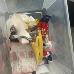 Mystery godis papper  - Bilderna visar en plastlåda med tomma godisförpackningar och papper, bland annat från Snickers, Dumle och andra godissorter. Ingen elektronikprodukt syns på bilderna.