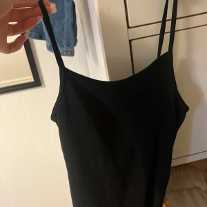 Svart klänning med smala axelband H&M - Enkel och stilren svart klänning från H&M med smala axelband. Modellen är rak och kort, perfekt för dig som gillar minimalistisk stil. Materialet känns mjukt och följsamt mot kroppen. Snygg att styla med sneakers eller klackar.