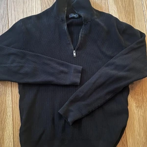 Svart zip-tröja från Mango  - Svart ribbstickad tröja från Mango med half zip-dragkedja och hög krage. Långärmad och i en klassisk, normal passform. Perfekt för lager-på-lager och enkel att matcha med jeans eller kjol.