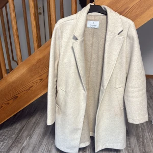 Beige kappa från Stradivarius - Snygg beige kappa från Stradivarius i storlek L. Klassisk rak modell med krage och två fickor framtill. Jackan har lång ärm och är tillverkad i mjukt material som ger en stilren look. Perfekt för dig som gillar minimalistisk och clean stil.