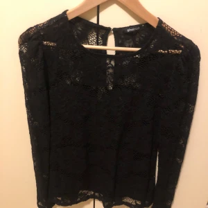 Svart spetsblus från Gina Tricot - Säljer en svart långärmad blus från Gina Tricot i genombruten spets med blommigt mönster. Blusen har rund halsringning och knapp i nacken. Perfekt för dig som gillar en elegant och trendig look.