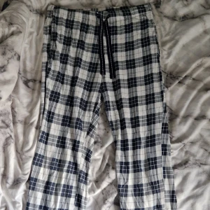Rutiga mjukisbyxor / pyjamasbyxor med snörning - Snygga mjukisbyxor i vitt och mörkblått rutigt mönster. Byxorna har elastisk midja med mörkblå snörning och är tillverkade i mjukt bomullstyg. Perfekta för chill dagar hemma, sova i eller när du vill vara extra bekväm. Säljer då dom är för korta för mig.