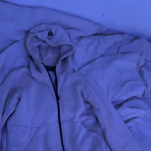 Beige fleecejacka från Sail Racing - Beige fleecejacka från Sail Racing med huva och hel dragkedja framtill. Jackan har en enkel och clean design med diskret logga på huvan. Perfekt för kyliga dagar när du vill vara både bekväm och snygg.