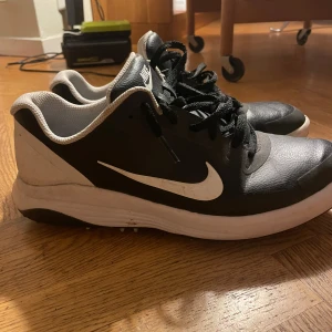 Nike Fitsole svarta golfskor - Svarta och vita Nike Fitsole sneakers i storlek 42,5. Skorna har används en del vilket syns på smutsfläckarna som lätt går att ta bort med vatten och diskmedel. I övrigt är de fortfarande i bra skick och snygga. Köpta nya för ca 800, säljer för 300.