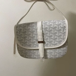 Vit axelväska med mönster - Säljer en snygg vit axelväska med ikoniska grafiska mönster. Väskan har justerbar axelrem, magnetlås och detaljer i vitt skinn. Insidan är fodrad i gult tyg och har flera fack för smart organisering. Kommer med dustbag, box och äkthetskort.