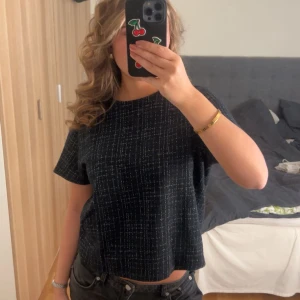Svart rutig topp med kort ärm - Säljer en svart topp med vitt rutmönster och korta ärmar. Toppen har en boxig, loose passform och är något croppad. Perfekt till jeans eller kjol för en chill look. Materialet känns mjukt och bekvämt mot huden.