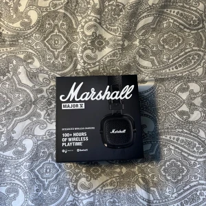 Marshall Major V - Marshall Major V är trådlösa on-ear hörlurar med över 100 timmars batteritid, Bluetooth, integrerad trådlös laddning och vikbar design. Ikonisk Marshall-ljudkvalitet och anpassningsbar knapp. Produkten och förpackningen är i nyskick utan synligt slitage.
