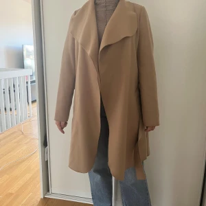 Beige kappa från Vila med bälte - Säljer en snygg beige kappa från Vila i storlek S. Stor krage och skärp. Kom gärna med bud!