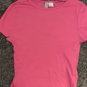 Rosa ribbad topp från Divided XS - Säljer en rosa ribbad topp från Divided i storlek XS. T-shirten har korta ärmar och rund halsringning. Perfekt för dig som gillar en enkel men snygg stil. Materialet är mjukt och stretchigt för en bekväm passform.