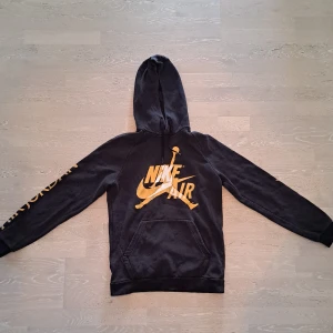 Svart Nike Air Jordan hoodie M - Svart hoodie från Nike Air Jordan med stor gul logga på bröstet och texten AIR JORDAN längs ärmarna. Magficka framtill och huva med snörning. Mjuk insida och relaxed fit.
