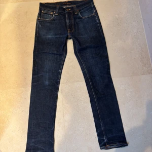 Nudie jeans  - Snygga mörkblå jeans från Nudie Jeans med klassisk femficksdesign och kontrastsömmar. Jeansen har raka ben och ikonisk broderad bakficka. Perfekta för dig som gillar stilrena och tidlösa jeans med en modern passform.