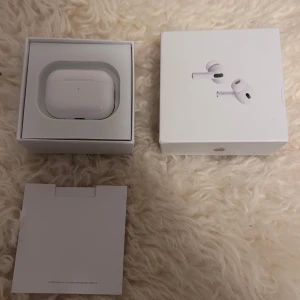 AirPods Pro 2 - Säljer ett par Apple AirPods Pro 2 i nyskick, komplett med originalkartong, extra öronkuddar och laddkabel. Produkten har begränsad garanti till maj 2026. Inga synliga defekter eller slitage, allt ser ut som nytt och oanvänt.