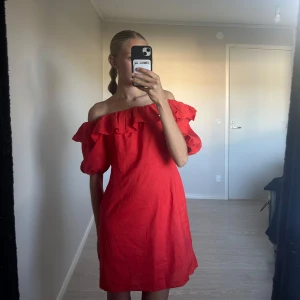 Röd offshoulder klänning med volang - Superfin röd kortklänning från H&M i linneblandning. Offshoulder-modell med volang runt hela ringningen och puffiga korta ärmar. Klänningen har dragkedja i sidan och en tajt passform, dock är den för stor för mig. 