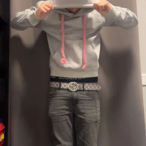 Ljusgrå hoodie med rosa snören - Säljer en ljusgrå hoodie med stora, grova rosa snören och huva. Tröjan har en klassisk känguruficka framtill och ribbade muddar vid ärmslut och nederkant. Perfekt för dig som gillar en chill och trendig stil.