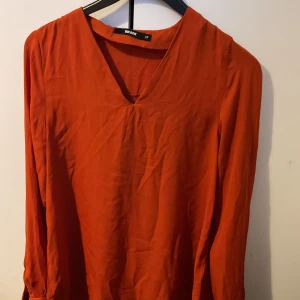 Rostfärgad blus från Bik Bok - Säljer en snygg rostfärgad blus från Bik Bok i storlek XS. Blusen har v-ringning och långa ärmar, perfekt för dig som gillar en enkel men trendig look. Materialet känns lätt och luftigt, vilket gör den skön att bära.