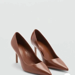 Bruna pumps - Snygga bruna pumps med klack. Skorna har en stilren design i glansigt skinnmaterial och en klassisk siluett som ger en elegant look. Skorna är helt oanvända i storlek 39 ,ordinarie pris 529kr