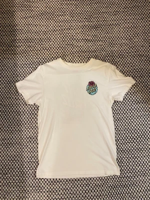 Vit Santa Cruz t-shirt med kaktusprint - Vit t-shirt från Santa Cruz i bomull med färgglad kaktusprint och logga på både bröstet och ryggen. Klassisk rund hals och korta ärmar. Trycket har inslag av blått, rosa och gult som ger en cool vibe.