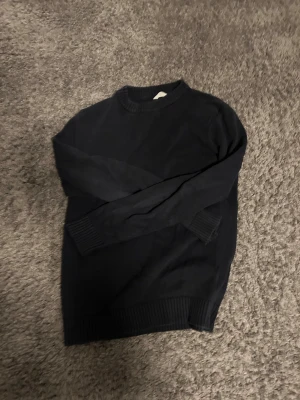 Mörkblå stickad tröja från Dobber - Säljer en mörkblå stickad tröja från Dobber i klassisk modell. Tröjan har rund hals, ribbade muddar vid ärmslut och nederkant samt lång ärm. Perfekt till höst och vinter för en clean och enkel stil.