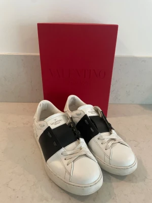 Valentino Garavani Open sneakers - Snygga Valentino Garavani Open sneakers i vitt skinn med bred svart läderdetalj över vristen och  nitar baktill på sulan. Kommer med originalkartong och dustbag. 