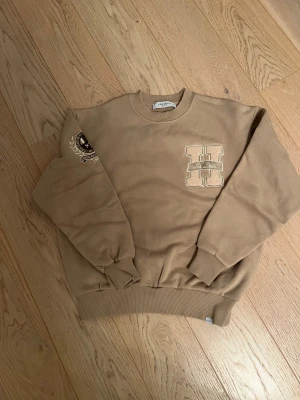 Les deux tröja - Snygg tröja från les deux, den är beige med en logga på bröstet. Den har en patch på höger arm. En väldigt skön tröja.