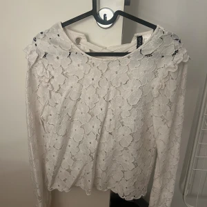 Vit spetsblus med snörning från hm - Supersöt vit blus från hm med blommigt spetsmönster och snygg snörning i ryggen. Långärmad modell med volangdetaljer vid axlarna och rundad hals. Perfekt för dig som gillar romantisk och feminin stil.