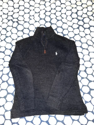 Mörkgrå half zip tröja Polo Ralph Lauren - Mörkgrå långärmad tröja från Polo Ralph Lauren i storlek XS. Tröjan har en klassisk half zip-dragkedja med läderdetalj och broderad logga på bröstet. Perfekt för lager-på-lager och chill stil under höst och vinter.