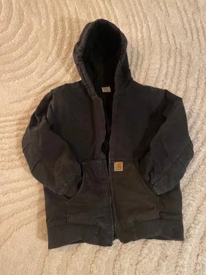 00s Vintage Carhartt Jacka - Svart Active från Carhartt i storlek XXS/XS, med quiltat foder och två stora fickor framtill. Jackan saknar dragkedja och har ett litet defekt vid midjan. Säljes pga för liten för mig Pris kan diskuteras