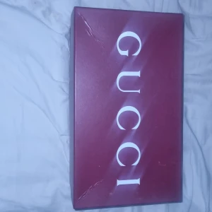 Gucci vita sneakers med röd/grön detalj - Säljer ett par fräscha vita sneakers från Gucci med klassisk röd och grön rand på sidan. Skorna har rund tå, platt sula och snörning. Tillverkade i skinn och levereras med originalkartong, extra skosnören och dustbag. Perfekt för dig som gillar lyxiga och stilrena sneakers.