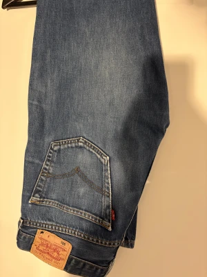 Levi's 501 blå jeans straight fit - Klassiska blå Levi's 501 jeans med rak passform och femficksdesign. Jeansen har den ikoniska läderpatchen bak, knappgylf och snyggt tvättad denim. Det perfekta jeans skicket. Rekommenderas för dig som är 180+ cm! Hör av dig vid frågor. W30/32 L32