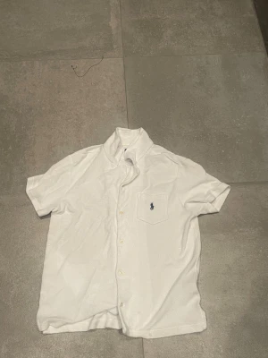 Frotté skjorta från Polo Ralph Lauren.  - Vit kortärmad frotté skjorta från Polo Ralph Lauren. Köpt från nk med kvitto. Köpte den för 2300 använd några gånger men behöver bli av med kläder