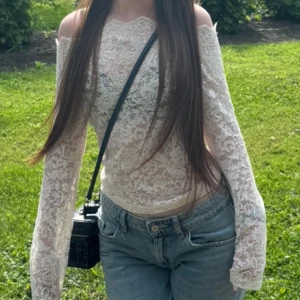 Vit spetsig offshoulder blus - Säljer en superfin vit blus i spets med offshoulder och långärmad design. Blusen har ett romantiskt mönster och är figurnära med lätt transparent material. Perfekt för dig som gillar detaljer och vill sticka ut med en feminin look.