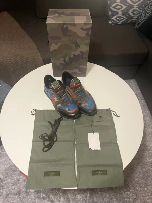 Valentino Rockrunner - Säljer ett par Valentino Rockrunner sneakers med grymt camouflagemönster i blått, rött, beige och svart. Skorna har detaljer i mocka och skinn. Kommer med originalbox, dustbags, extra snören, tag och valentino brev. Perfekt för dig som vill ha ett par feta dojor för vintern. Självklart äkta, kan skicka extra bilder på allt, svarar snabbt på frågor. 
