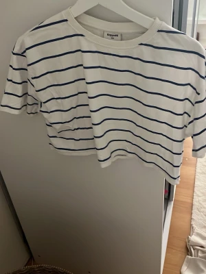 Vit och marinblå randig t-shirt Kappahl - Snygg vit t-shirt från Kappahl med marinblåa ränder. Modellen är kortärmad och har en klassisk rund halsringning med ribbad kant. 