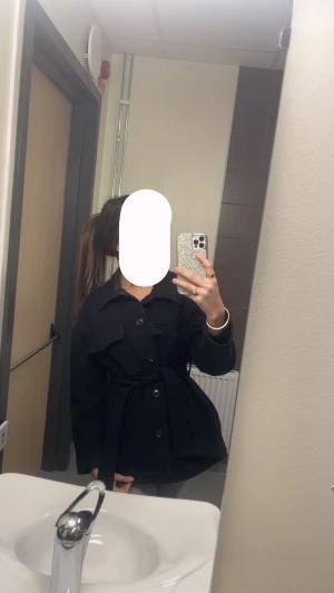 Svart kappa med bälte och knappar - Säljer en svart overshirt med snyggt bälte i midjan och stora knappar framtill. Jackan har klassisk krage och lång ärm, perfekt för lager-på-lager. Stilren och enkel att matcha med olika outfits.