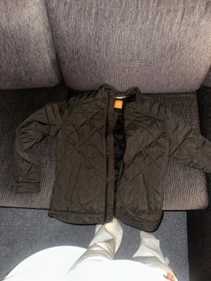 Svart pufferjacka Hugo BOSS - Säljer en svart quiltad pufferjacka från Hugo BOSS, storlek M, Orange med dragkedja framtill och diskret logga på ärmen. Materialet är syntet och jackan är lätt vadderad.