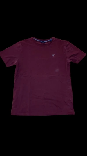Vinröd GANT t-shirt i bomull - Snygg vinröd t-shirt från GANT med klassisk rund hals och korta ärmar. T-shirten har ett broderat GANT-logo på bröstet och är gjord i mjuk bomull. Perfekt för dig som gillar stilrena och bekväma plagg.