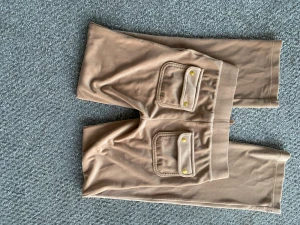 Juicy byxor  - Snygga beige mjukisbyxor från Juicy Couture med bred resår i midjan och guldfärgade detaljer på snörningen. Byxorna har raka ben, stora fickor fram med broderad logga och guldknappar på bakfickorna. Mjukt och skönt material som ger en chill vibe.