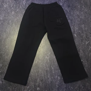 Saint Alexander Sweatpants svart S/M - Stilrena och bekväma sweatpants från Saint Alexander i klassiskt svart. Gjorda i mjukt och skönt bomullsmaterial med resår och dragsko i midjan för justerbar passform. Utrustade med sidfickor och har en modern, avslappnad fit som passar perfekt både till vardags och chill. Perfekta för en clean streetwear-look eller en bekväm dag hemma.