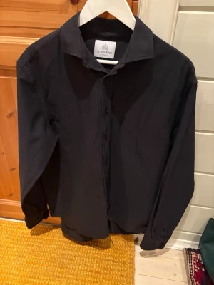 The Shirt Factory skjorta - En svart skjorta från The Shirt Factory. Använd endast en gång och nypris är runt 1300. Inga skavanker och extra knapparna finns kvar. Har bara hängt på galge. Är en strykfri skjorta men har några skrynklor då den bara hängt med kan stryka om det behövs. Hör av dig vid frågor!