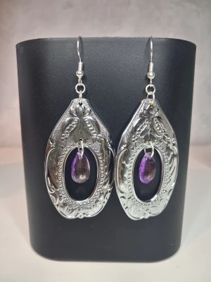 Egentillverkade örhängen återbruk  - Handgjorda örhängen skapade av en tång i krom/metall. Örhänget pryds av en lila transparent pärla med lite guldskimmer i som är formad som en droppe. Längd ca 5cm blir en unik och elegant accessoar till outfiten. Öronkroken är nickelsäker och aldrig använd 
