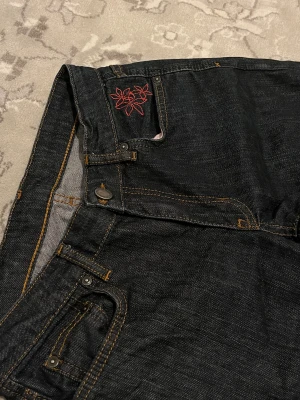 Svarta jeans från GANT med broderi vid fickan - Säljer dessa jättefina jeans i en djup och snygg mörkblå denimfärg från GANT. De har en fin detalj med en liten broderad blomma i rött/rosa på myntfickan (se bild). Jeansen är märkta med barnstorlek XXL (158–164 cm / 13-14 år), men jag som är 163 cm och normalt använder XS/S eller storlek 34 i vuxenstorlekar passar dem perfekt! Passformen är rak/lätt bootcut. De är i bra skick och har en materialblandning med 2% elastan vilket gör dem sköna och stretchiga. Ett par klassiska märkesjeans i en fin 