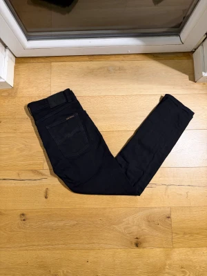  Nudie Jeans Lean Dean - Svarta jeans från Nudie Jeans i modellen 31/30. Jeansen har klassisk femficksdesign, svarta sömmar och Nudie Jeans logga på bakfickan. Tillverkade i ekologisk bomull med en straight passform som sitter snyggt. Perfekta för dig som gillar stilrena och enkla jeans.