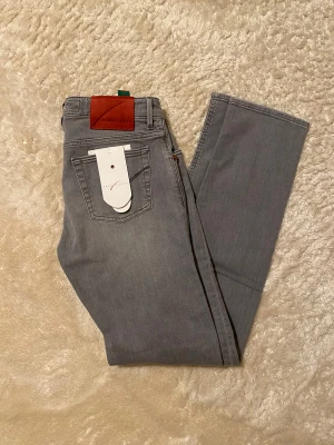 Grå jeans från Handpicked, straight fit - Snygga grå jeans från Handpicked med klassisk femficksdesign och raka ben. Jeansen har en diskret logga på bakfickan och gröna detaljer i midjan. Passar dig som gillar stilrena och enkla jeans med modern touch. Nya med tag, kontakta vid frågor.