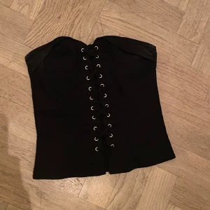 Svart korsett med snörning och dragkedja - Asnygg axelbandslös korsettopp med snörning och dragkedja baktill