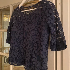 Mörkblå spetsblus från Pimpinette - Säljer en mörkblå blus från Pimpinette med blommigt spetsmönster och trekvartsärm. 