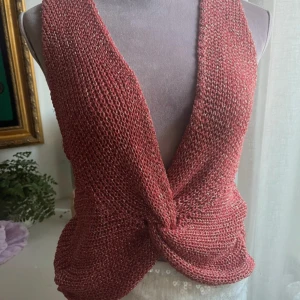 Glittrig vinröd omlott linnetopp - Säljer en stickad vinröd linnetopp med glittriga inslag och omlott-detalj framtill. Toppen är ärmlös och har en djup v-ringning som ger en snygg siluett. Materialet är mjukt och har en skimrande finish som syns tydligt i ljuset. Perfekt för dig som gillar att sticka ut.