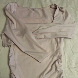 Ljusrosa långärmad topp - Snygg ljusrosa topp med lång ärm och fyrkantig urringning. Modellen är figurnära med rynkade detaljer längs sidorna för en cool siluett. Mjukt och stretchigt material som känns skönt mot huden. Perfekt för dig som gillar stilrena och feminina plagg.
