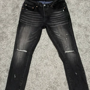 Svarta jeans från Purple Brand - Säljer ett par riktigt feta jeans från Purple Brand i storlek 30x32 med slim passform och slitna detaljer vid knäna. Jeansen har en tvättad look med ljusare partier och små vita färgstänk på framsidan. Klassisk femficksmodell och läderpatch med logga bak i midjan. Nypris runt 2500kr 