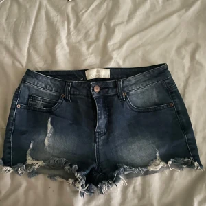Lågmidjade jeansshorts från pieces💕 - Snygga blå lågmidjade korta jeansshorts från pieces med fransig och sliten kant. Klassisk femficksmodell med knapp och dragkedja framtill. Shortsen har en mörk tvätt och slitningar både fram och bak.🤩Säljer då de är lite för små för mig. Står inte storlek men skulle gissa S/M.💕