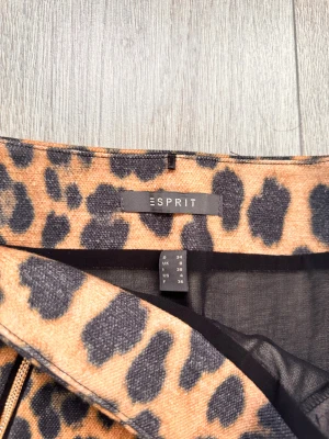 Leopardmönstrad kortkjol från Esprit - Snygg kortkjol från Esprit med leopardmönster i bruna och svarta toner. Kjolen har två framfickor med guldfärgade dragkedjor och är tillverkad i ett mjukt, vävt material som ger en cool vibe. Perfekt för dig som gillar att sticka ut med djurmönster.